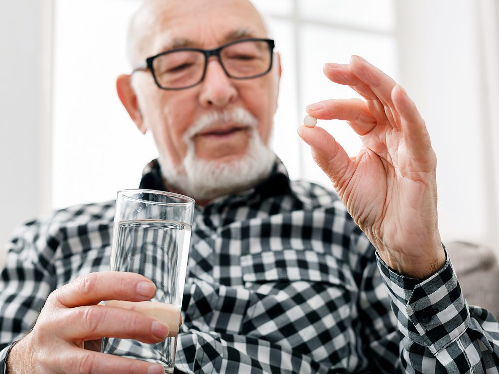 older man with medication and glass of water
