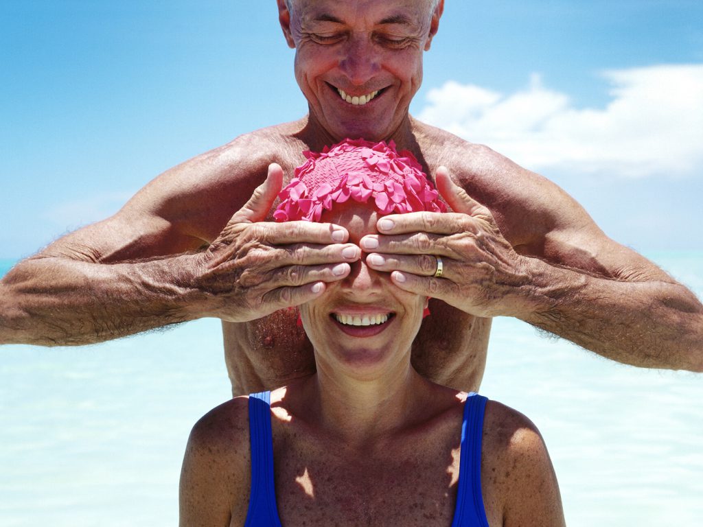 man covering woman's eyes on beach