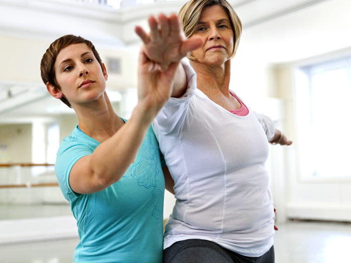 fitness instructor assisting woman with yoga pose