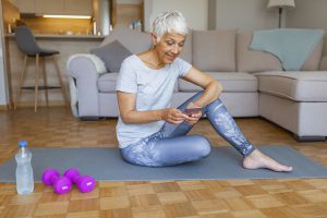 Older woman using smartphone after sports training sitting indoors at home.