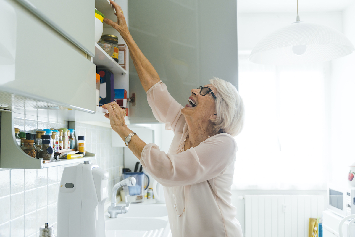 mujer mayor tratando de alcanzar algo del armario de cocina