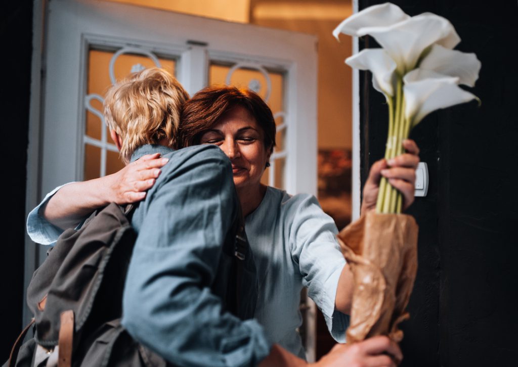 Senior woman hugging someone at the door with a bunch of flowers